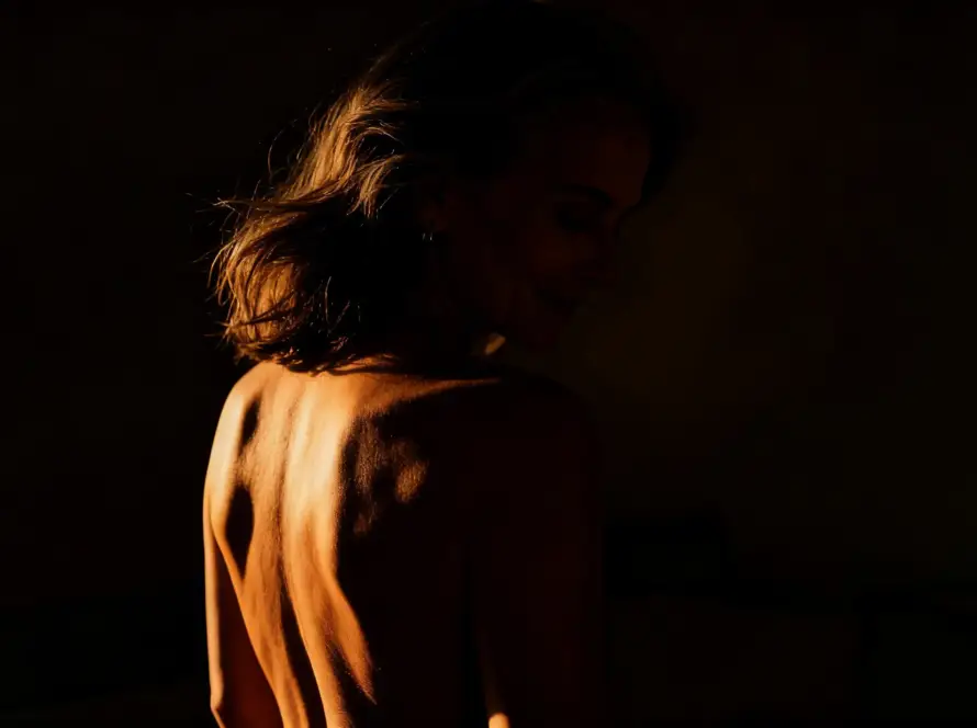 Perfil de mujer madura con luz dorada sobre hombro desnudo, presencia erótica y consciencia corporal. Tántrika™.