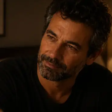 Marcos mirando a Isabel en la penumbra cálida de su cuarto, la mirada de quien acaba de descubrir un idioma nuevo en alguien que conoce de memoria — Serie Sexualidad Tántrica Tántrika™